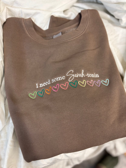 Brown sweatshirt with colorful text and heart symbols on a white background