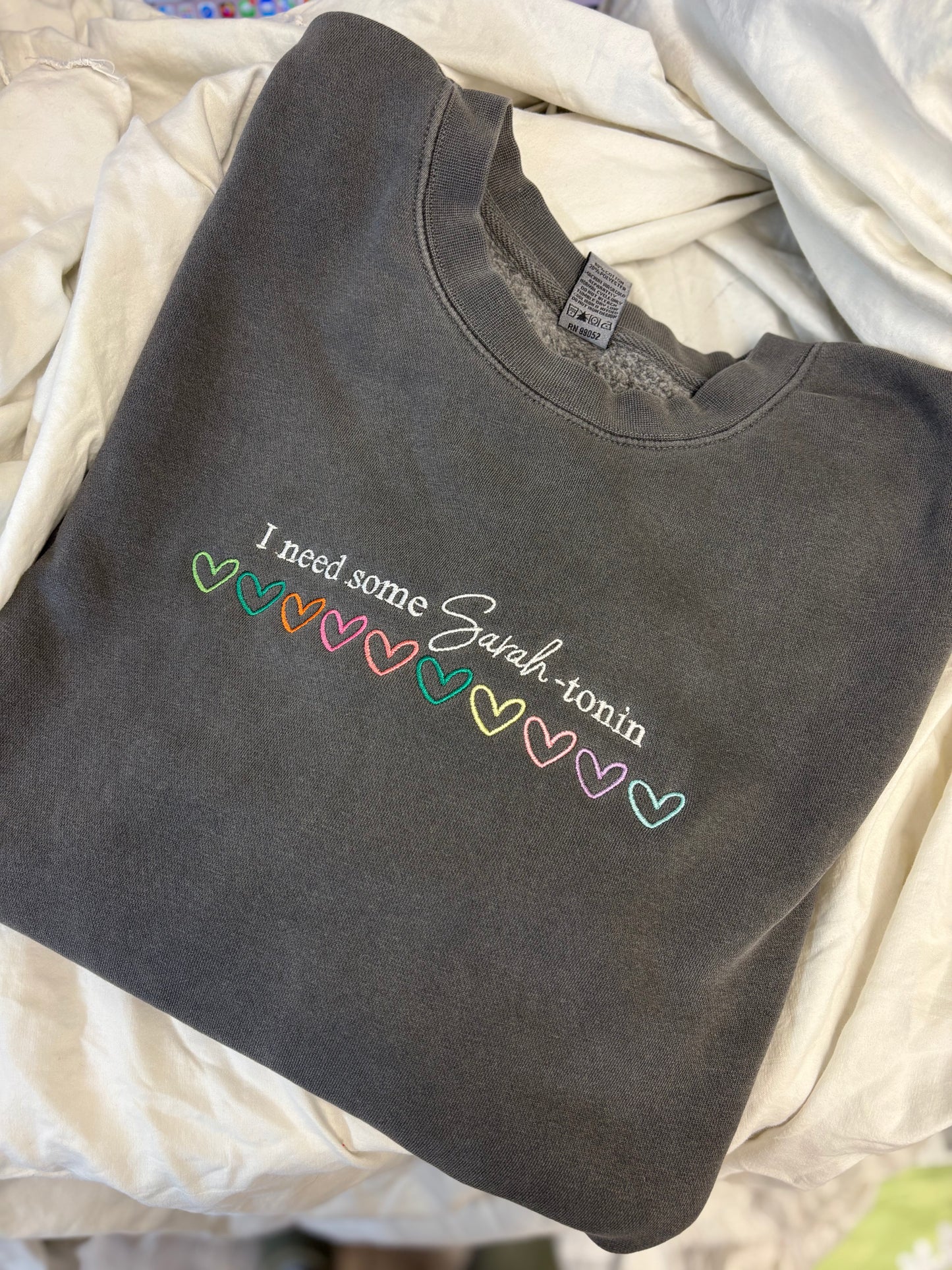 Dark gray sweatshirt with colorful text on a light beige blanket