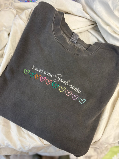 Dark gray sweatshirt with colorful text on a light beige blanket